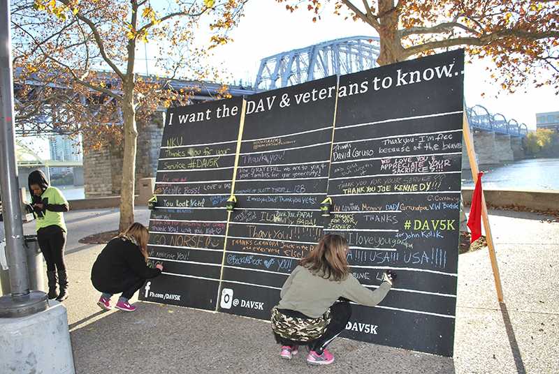 Participants write messages to veterans with chalk on Savickis wall. 