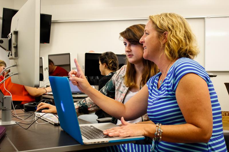 A professor works with a student in a Griffin hall classroom. The open desks and floor plan provides a more interactive classroom environment.
