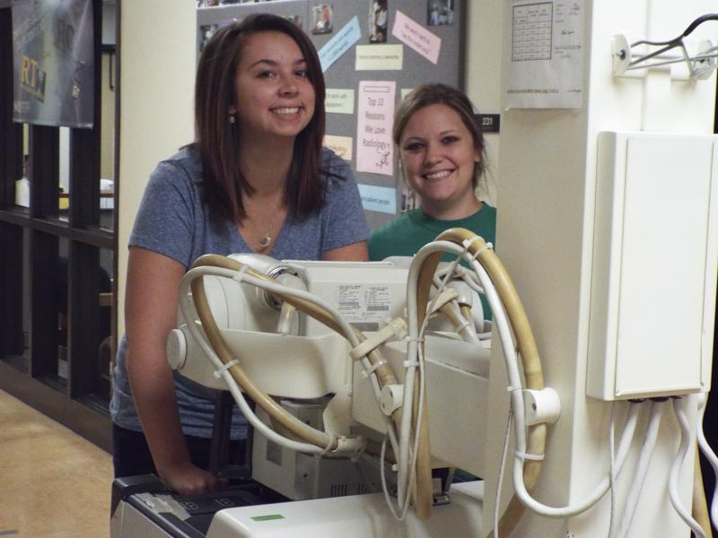 Sarah Listerman (left) and Sarah Reverman (right). They are pushing the mobile x-ray unit down the hallway outside of lab. 