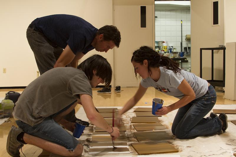 Sophomore Gabby Siekman, Kevin Muente and Jack Seiter paint tiles that are part of the piece. The exhibit runs until Oct. 30.