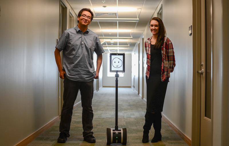 Austin Lee and Anne Thompson stand with Pineapple. The robot takes part in social robotics.