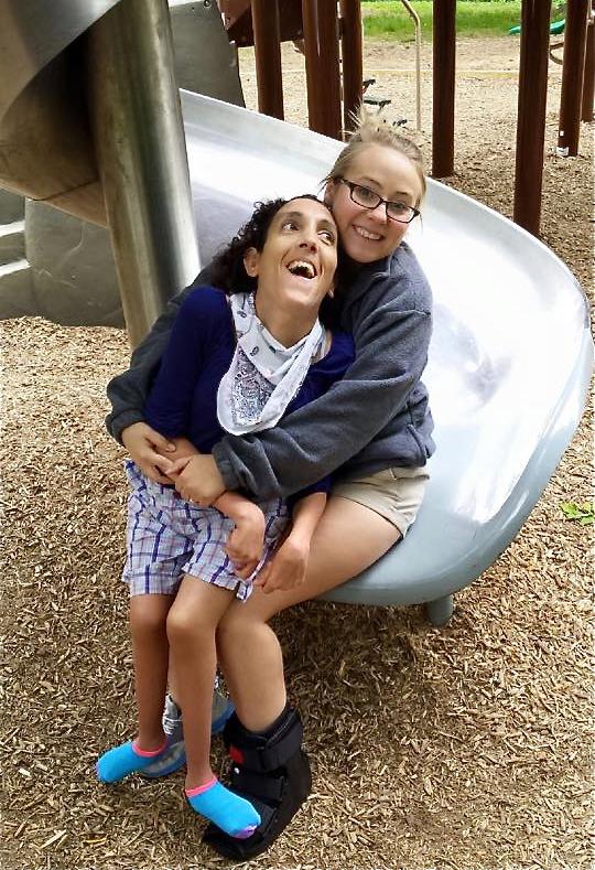 Justice helping her friend Brittany go down the slide. Brittany uses a wheelchair and cannot walk so Justice helps her by letting her sit on her lap.

