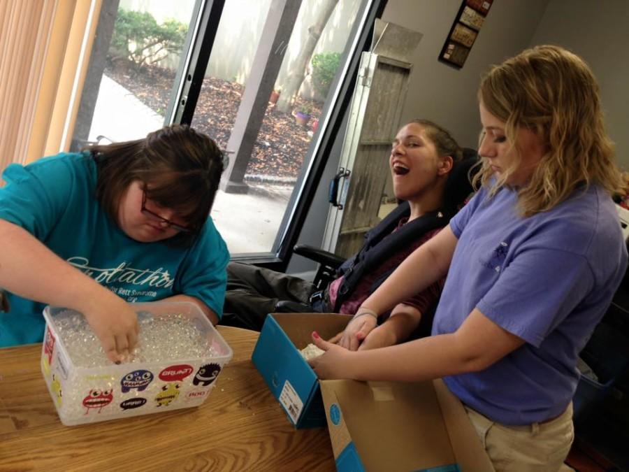 Justice working with Sarai and Toni on sensory activities - which help stimulate the use of their senses. Justice is helping Sarai with hand over hand to work on her sense of touch.