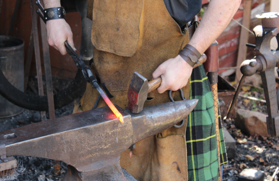 A blacksmith at the Dragons Forge shapes red-hot metal with a hammer and anvil.