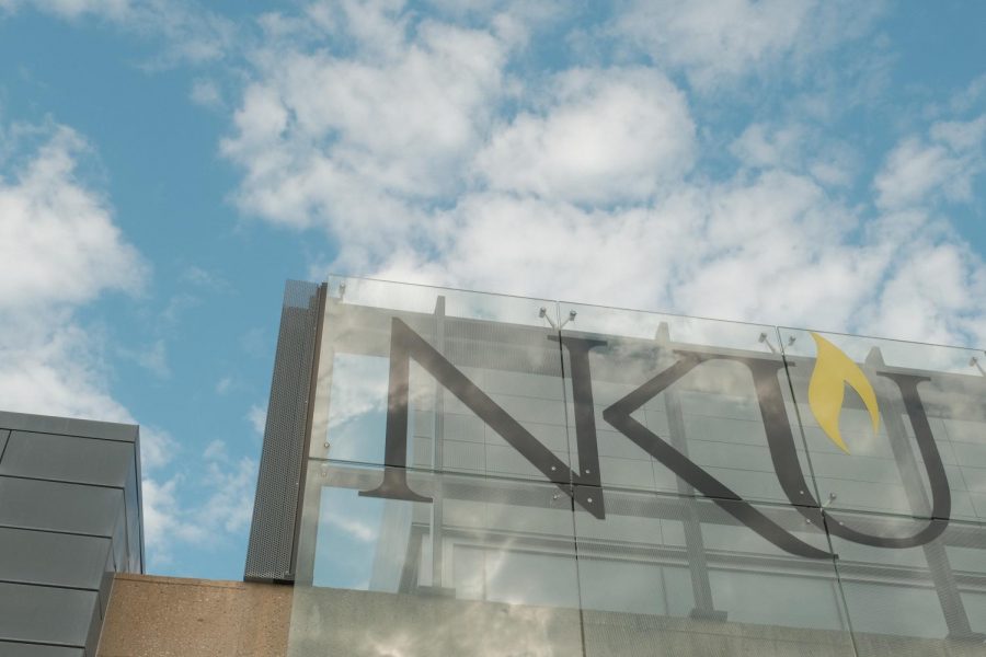 A sign that, in black text, says NKU. Clouds are in the sky.