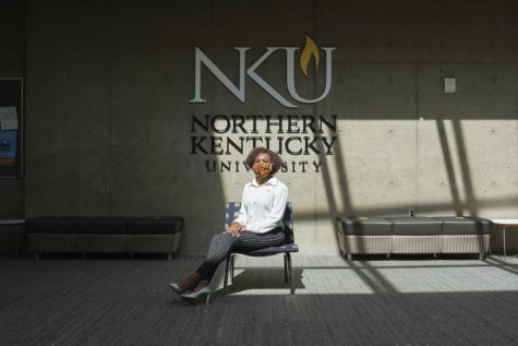 Kaitlin Minniefield sits on a chair in front of an NKU logo. She's wearing a white shirt and black pants.