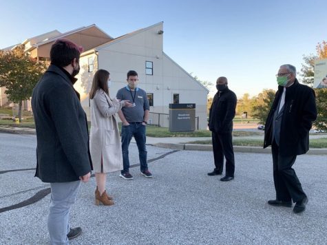 Goodwin outside wearing a coat and mask talking with others who are wearing masks. 