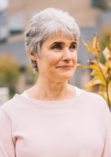 Joan Ferrante wearing a pink shirt staring off to the side of the camera.