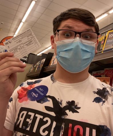 Freshman Jimmy Renton holding his COVID-19 vaccination record card while wearing a blue face mask.