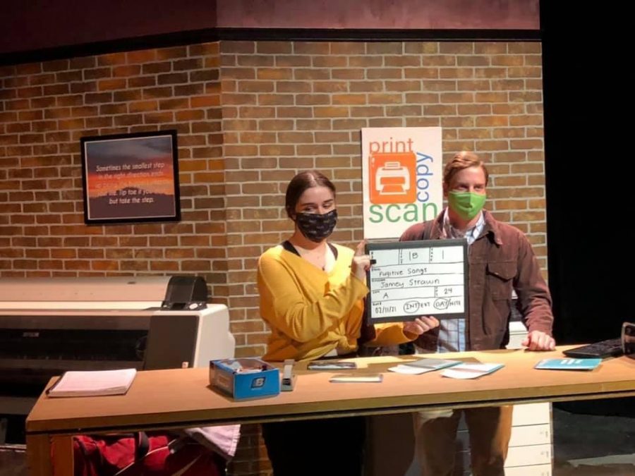 A woman in a yellow shirt and black face mask marks the scene standing next to a man in a brown shirt.