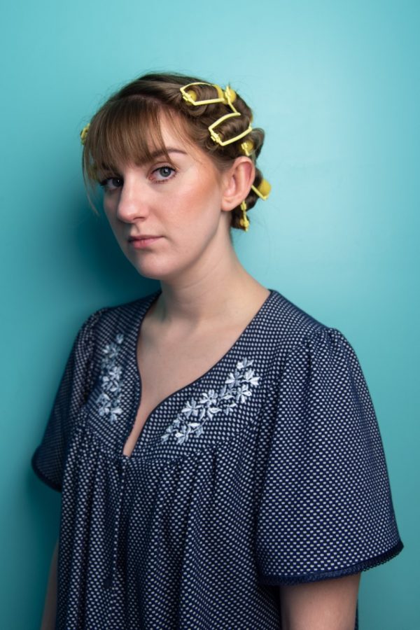 Jasmine looking at the camera with a straight face, wearing a blue shirt and hair is pinned up.