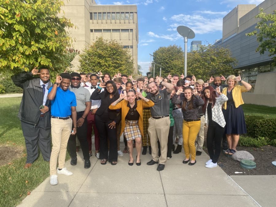 SGA members next to the SU after Mondays meeting. A large group of almost 30 members all doing the Norse up motion with their hands next to their heads.