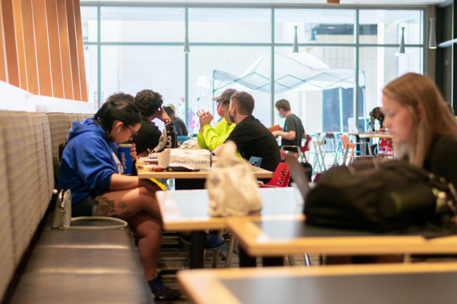 Students eating and talking to one another in the Student Union at tables spread out.