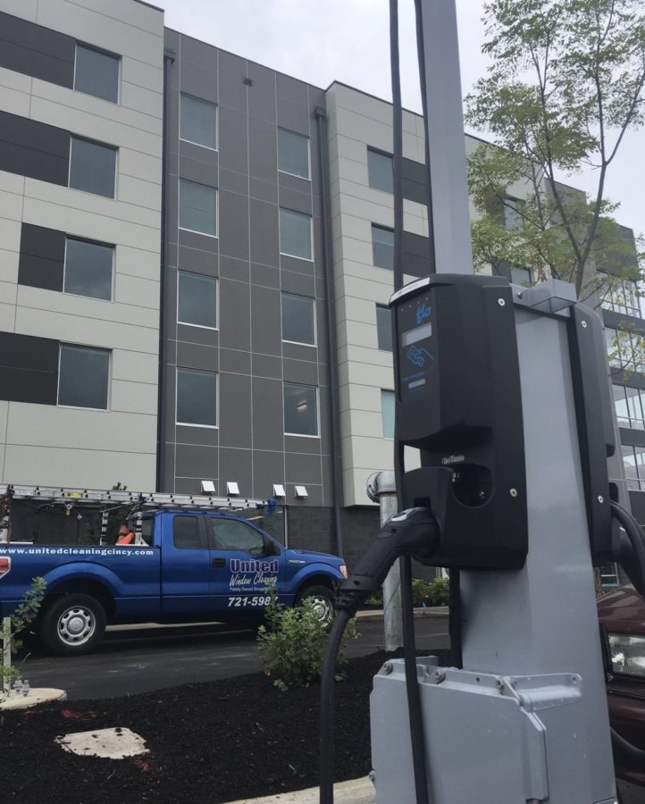 An electric vehicle charging station in foreground, building and blue pick-up in background