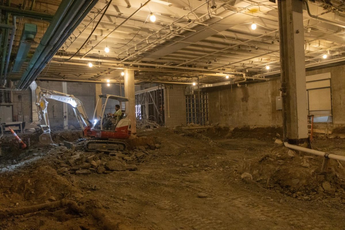 Construction worker operates excavator on first floor of the Fine Arts Center.